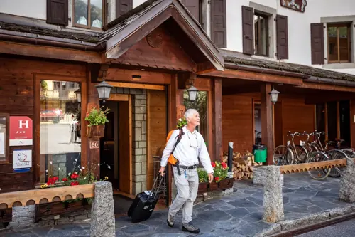 Older man leaving hotel, rolling suitcase behind him
