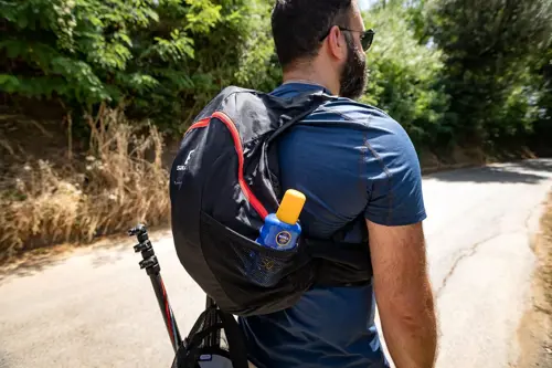 Man walking on trail with daypack, sunscreen and walking poles visible
