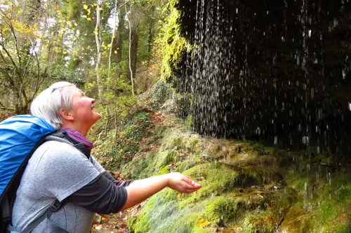 Older woman standing with hands cupped under a waterfall